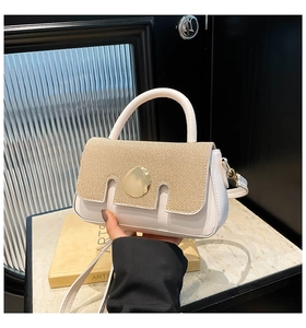 Close-up of elegant white leather handbag with woven straw flap and gold round buckle