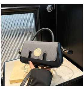Detail of grey twill and black leather handbag with gold round buckle and adjustable strap