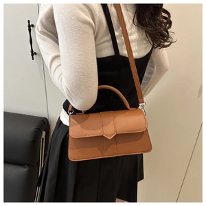 Brown leather handbag with geometric buckle shown on model in a minimalist setting