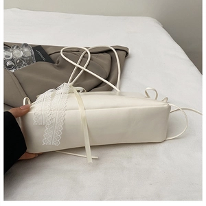 Detail of off-white faux leather shoulder bag featuring elegant white lace ribbon tie