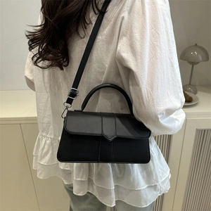 Minimalist black matte leather handbag with triangle flap and crossbody strap on a model