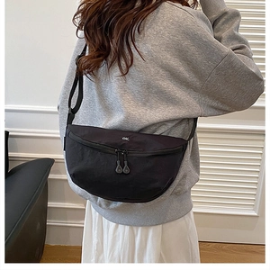 Sac bandoulière demi-lune noir en nylon avec broderie OK porté par un mannequin en jupe