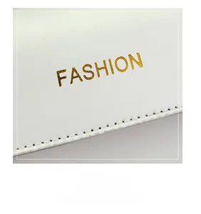 Nahaufnahme des goldenen FASHION-Logos auf weißem Leder mit präzisen, feinen Nähten