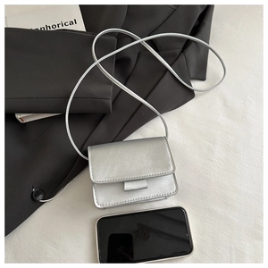 Close-up of a mini silver crossbody bag showing its metallic texture next to a smartphone