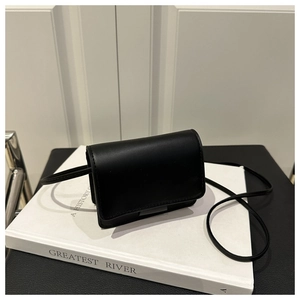 Detail of minimalist black leather crossbody bag with metal accent on a book