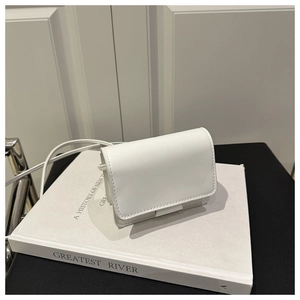 Detail shot of a white minimalist flap crossbody bag on a book with sleek stitching