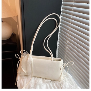 Detail of white rectangular shoulder bag featuring delicate lace bows and ribbon ties