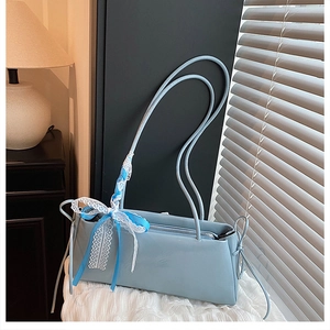 Detail of light blue faux leather baguette bag with a silk and lace bow on the shoulder strap