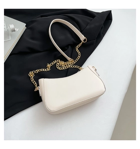 Top view of cream-colored baguette shoulder bag with gold chain and leather strap