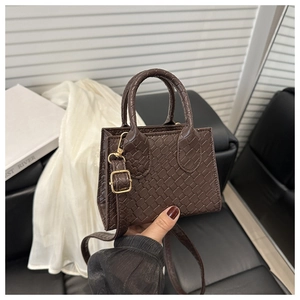 Detail of dark brown mini tote bag featuring woven texture and gold metal buckle