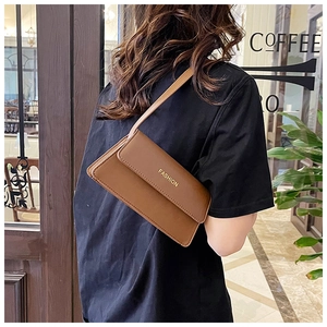 Braune Leder-Schultertasche mit Fashion-Logo, getragen von einem Model im Café
