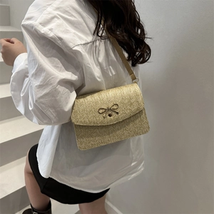 Sac bandoulière tissé beige avec fermoir nœud doré porté par un mannequin pour l'été