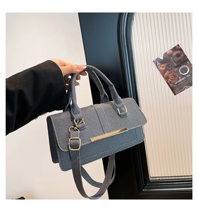 Detail of blue denim textured handbag featuring a gold bar buckle and round top handles