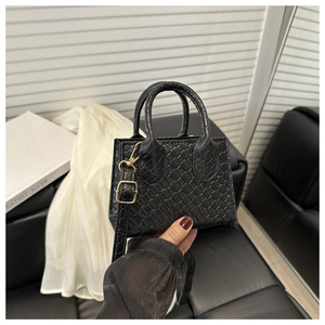 Detail of black woven handbag featuring gold hardware and adjustable shoulder strap