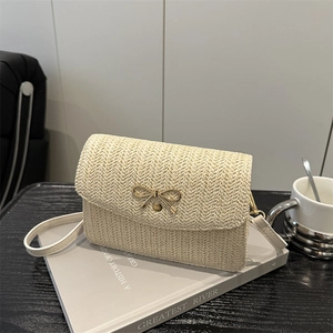 Sac bandoulière tissé crème avec nœud doré posé sur un livre au style minimaliste