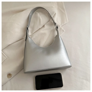 Macro detail of silver underarm bag with sleek crescent shape and phone size reference