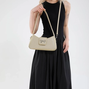 Elegant beige underarm bag with silver bow accent on model in black dress