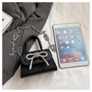 Dettaglio di una mini borsa in pelle nera con fiocco di cristallo e tracolla a catena
