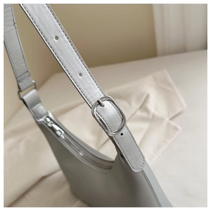 Detail of silver-toned adjustable buckle and smooth leather strap on a grey underarm bag