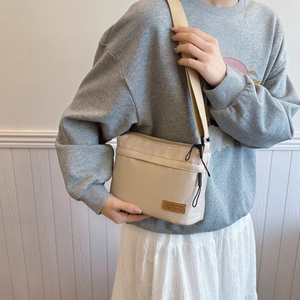 Minimalist beige nylon tote bag with wide adjustable strap shown in a front view