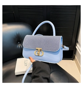 Detailed close-up of light blue leather handbag with gold CD clasp and denim texture