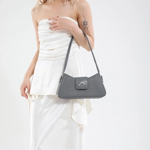 Elegant grey fabric baguette bag with silver bow accent worn by a model on white background