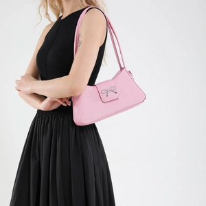 Pink minimalist shoulder bag with silver bow accent on a model over white backdrop