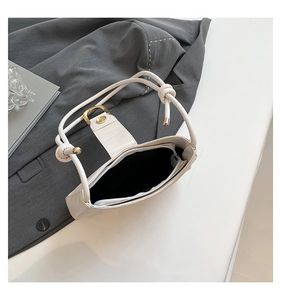 Close-up of white leather shoulder bag featuring a knotted handle and gold metal buckle detail