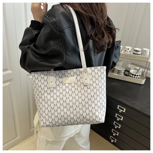 Close-up of white tote bag featuring grey M-pattern print and golden logo plate