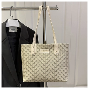Close-up of beige tote bag with grey M-letter pattern and gold FASHION metal plaque