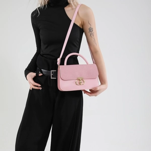 Pink crossbody bag with textured flap and gold buckle carried by a model in black outfit
