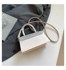 Close-up of minimalist white handbag with grey glitter flap and gold metal hardware detail