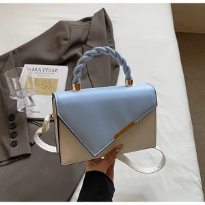 Detail of color-block handbag with gold hardware, twisted handle and a white strap