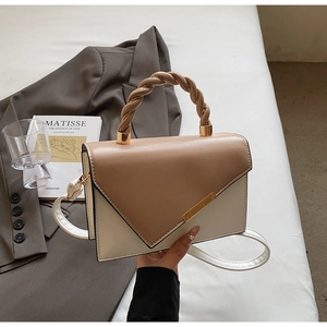 Detail of color-block handbag with twisted top handle and gold metal trim on grey suit