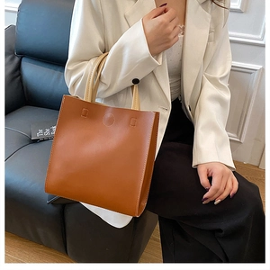 Detail of a brown leather tote bag with beige cylindrical handles and white topstitching