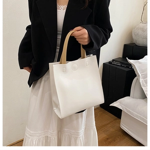 Minimalist white tote bag with contrasting brown handles shown in a lifestyle indoor setting