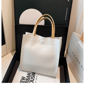 Detail of minimalist white tote bag featuring contrast ginger yellow handles and PU leather