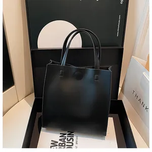 Detail of minimalist black leather tote bag featuring dual handles and magnetic closure