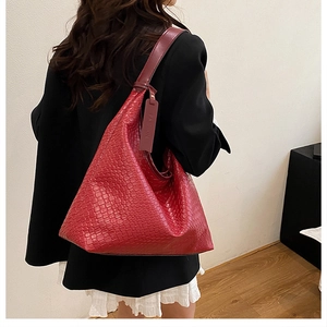 Detail of red oversized shoulder bag featuring woven texture and fashion charm