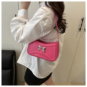 Détail d'un sac sous le bras rose vif avec un nœud métallique argenté et bandoulière