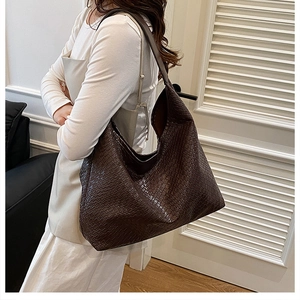 Detail of deep brown large tote bag featuring textured faux crocodile leather and wide strap