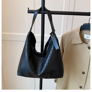 Detail of black woven leather hobo bag with wide shoulder strap and blue charm