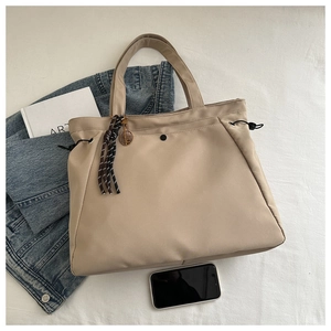 Flat lay of khaki nylon tote bag with drawstring details and woven fringe charm