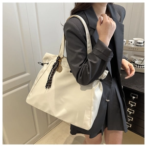 Detail of a large cream tote bag featuring a tennis racket charm and striped tassel accessory