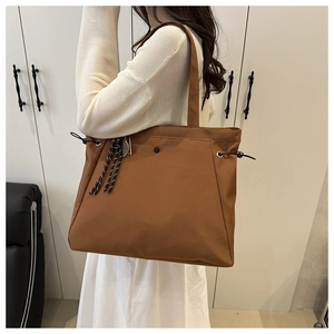 Detail of tan nylon tote bag showing side drawstrings and woven rope charm hanging