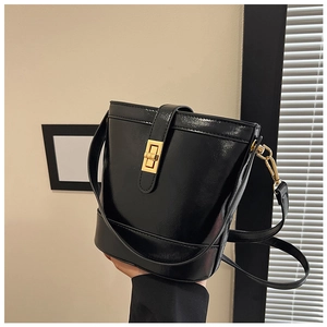 Detail view of a black glossy bucket bag with a golden turn-lock closure and shoulder strap