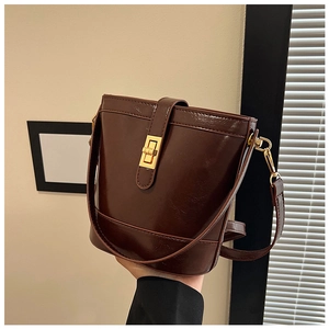 Detail of dark brown glossy bucket bag featuring gold rectangular twist lock and stitching