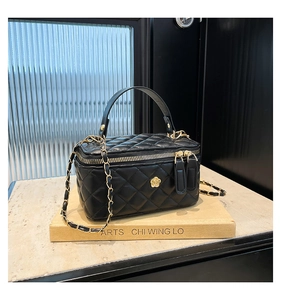 Detail of black quilted box bag with gold floral clasp and woven chain strap