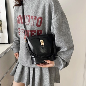 Minimalist black bucket tote bag with gold twist lock closure and leather shoulder strap