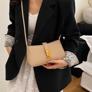 Minimalist beige shoulder bag for women with gold clasp worn by a model in a room